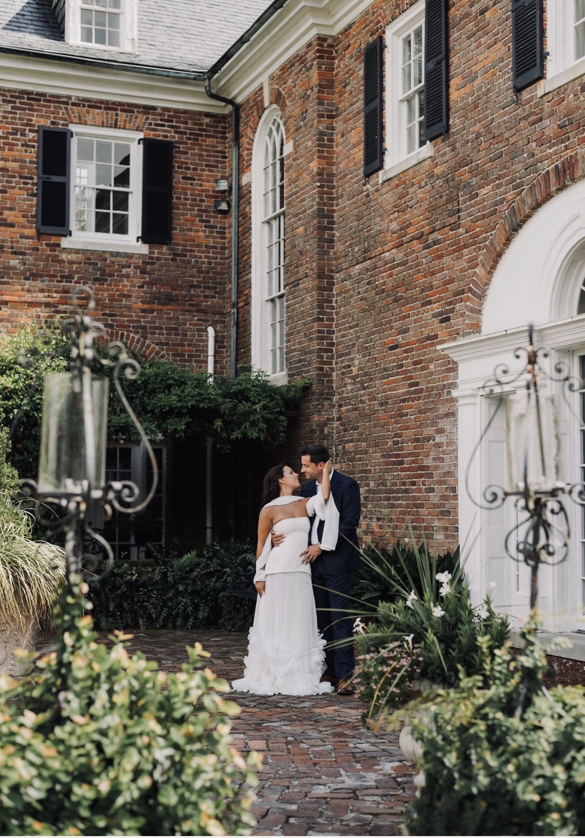 Chloe and Sam embracing in a courtyard framed by historic brickwork