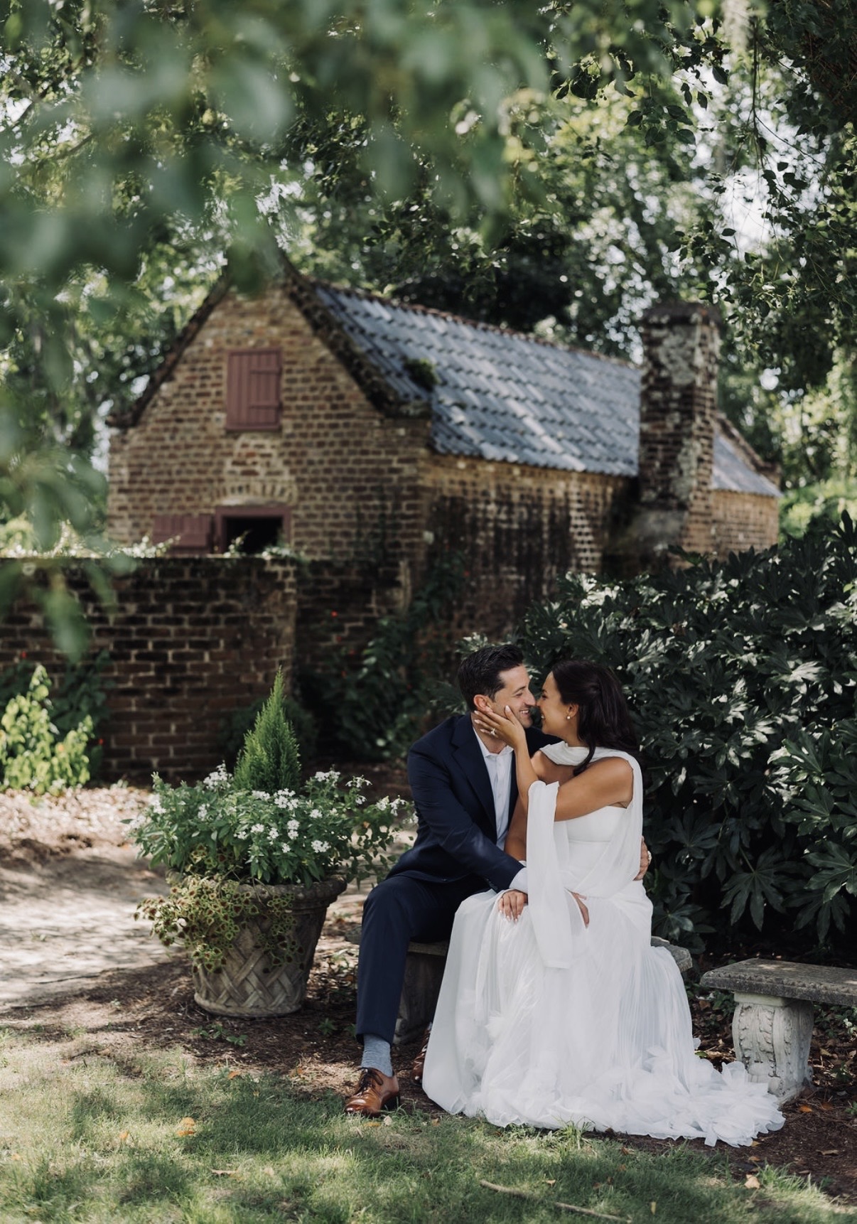 Chloe and Sam seated in a lush garden beside a historic brick cottage