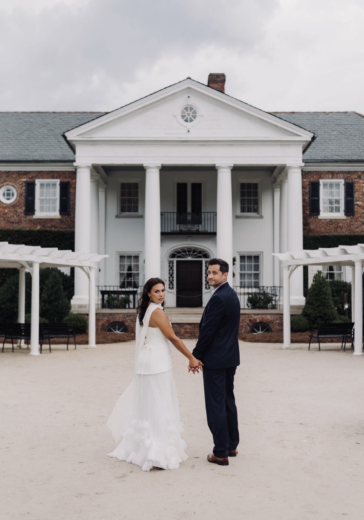 Chloe and Sam holding hands before a white-columned house
