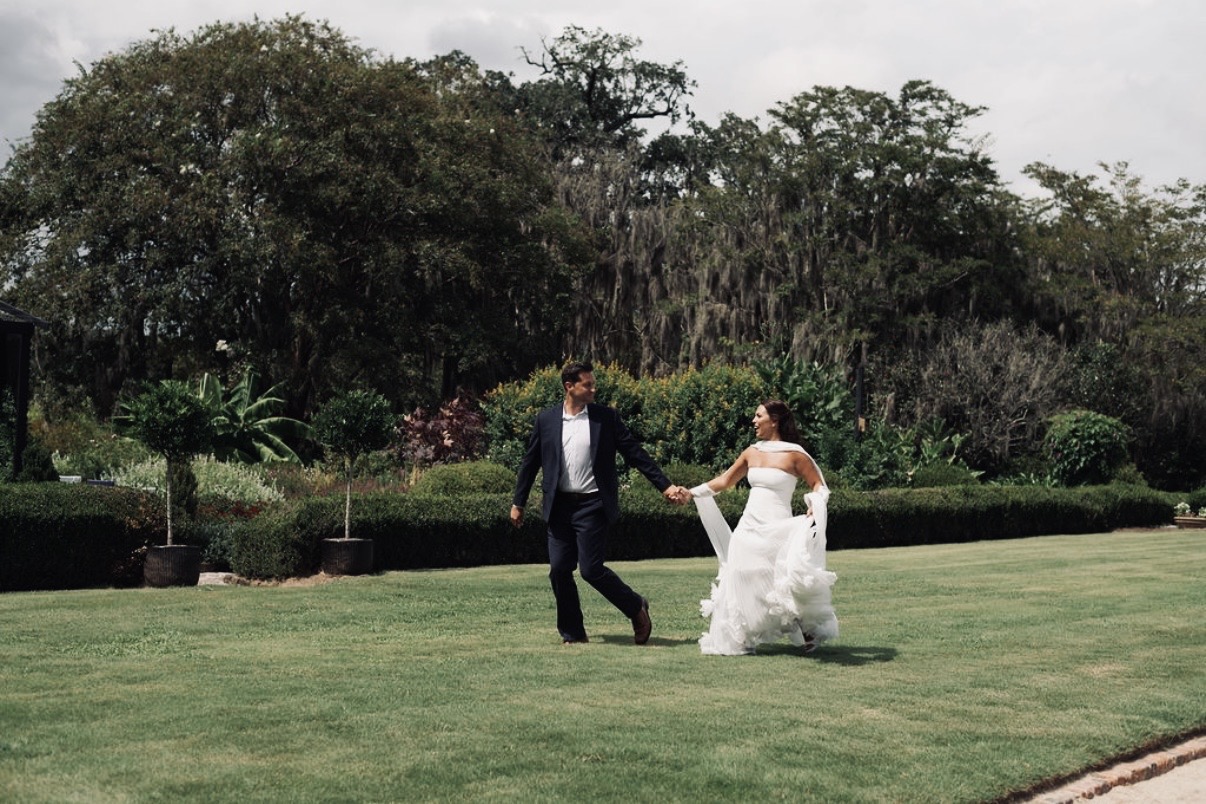 Chloe and Sam running hand in hand across a Charleston lawn